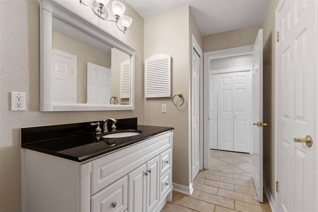 This well-maintained bathroom featuring a white vanity with black countertop, undermount sink, and a large mirror. There’s tiled flooring and the room has a neutral color scheme. It includes a towel ring and a light fixture above the mirror.