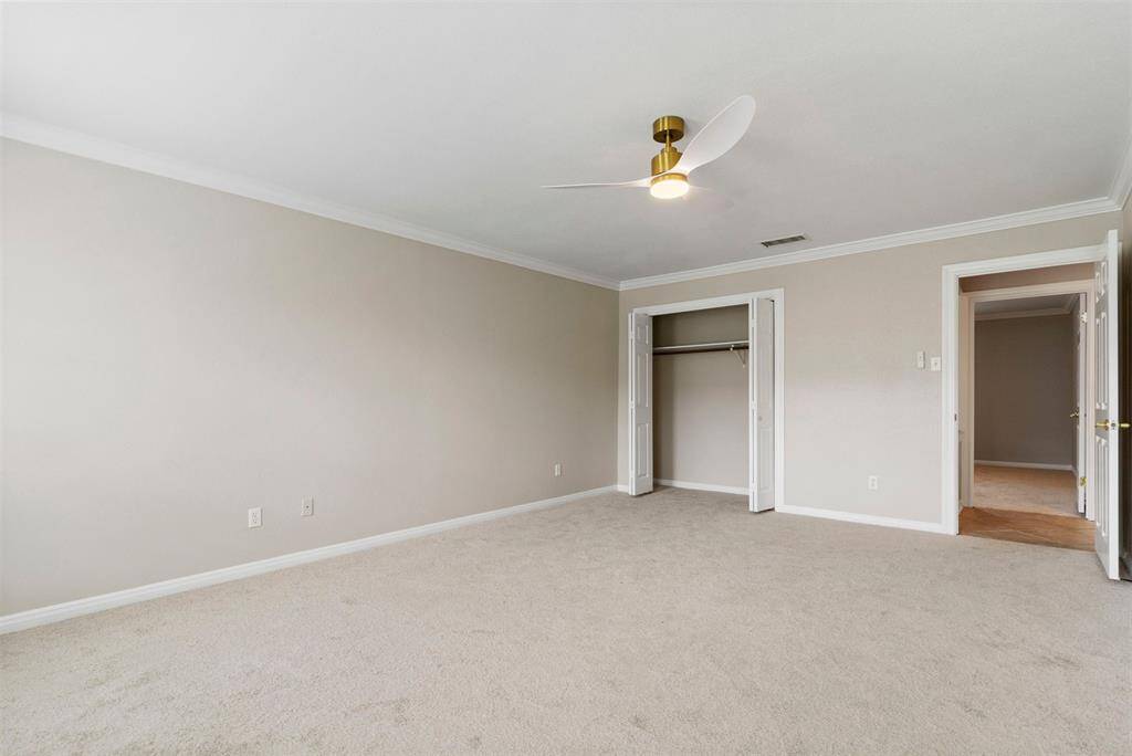 This is a spacious primary bedroom with neutral walls and new carpet flooring, featuring a new ceiling fan and two closets for ample storage.