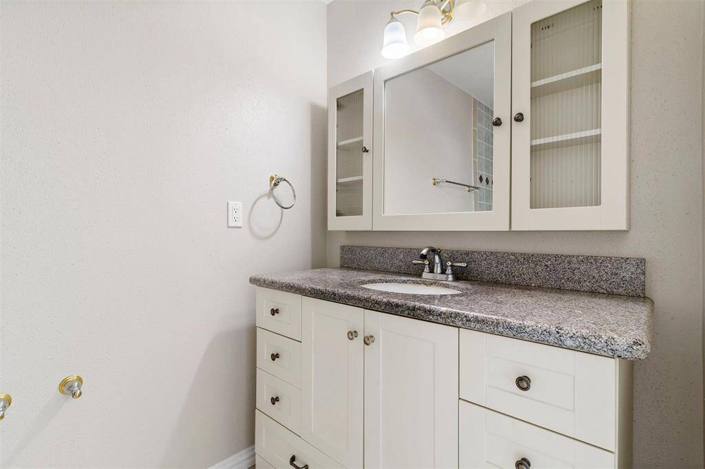 This bathroom featuring a white vanity with ample storage, a granite countertop, and a mirror cabinet above the sink.