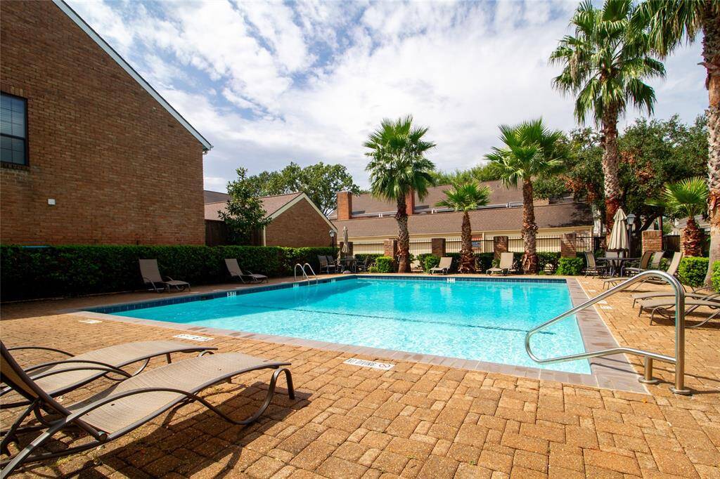 The communal outdoor swimming pool area with lounge chairs, surrounded by attractive brick residential buildings and landscaped with palm trees, providing a serene environment perfect for relaxation and entertainment.