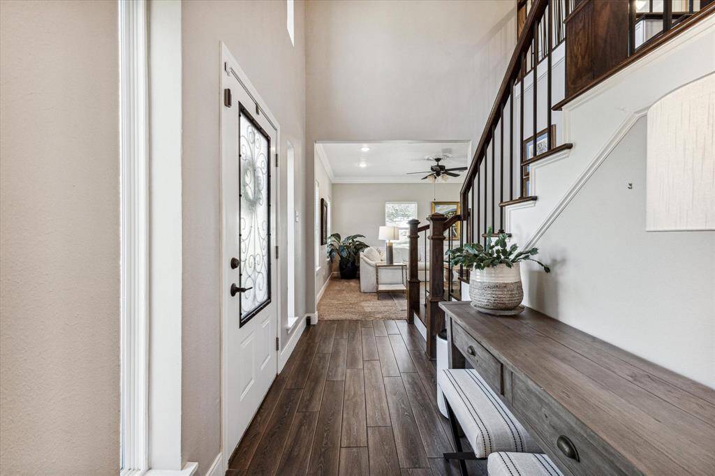 The stylish entryway features elegant wood-look flooring, a decorative front door, and a staircase with rich wood accents, seamlessly leading into the bright, inviting living area.