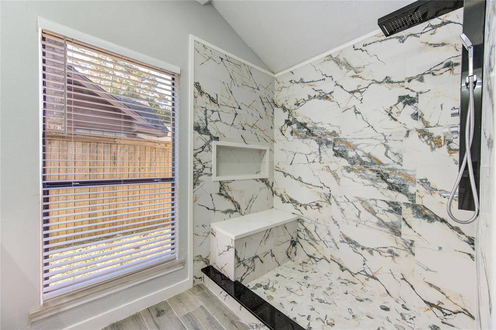 Luxurious primary bathroom shower featuring elegant marble-style tiles, a built-in bench, and sleek fixtures.