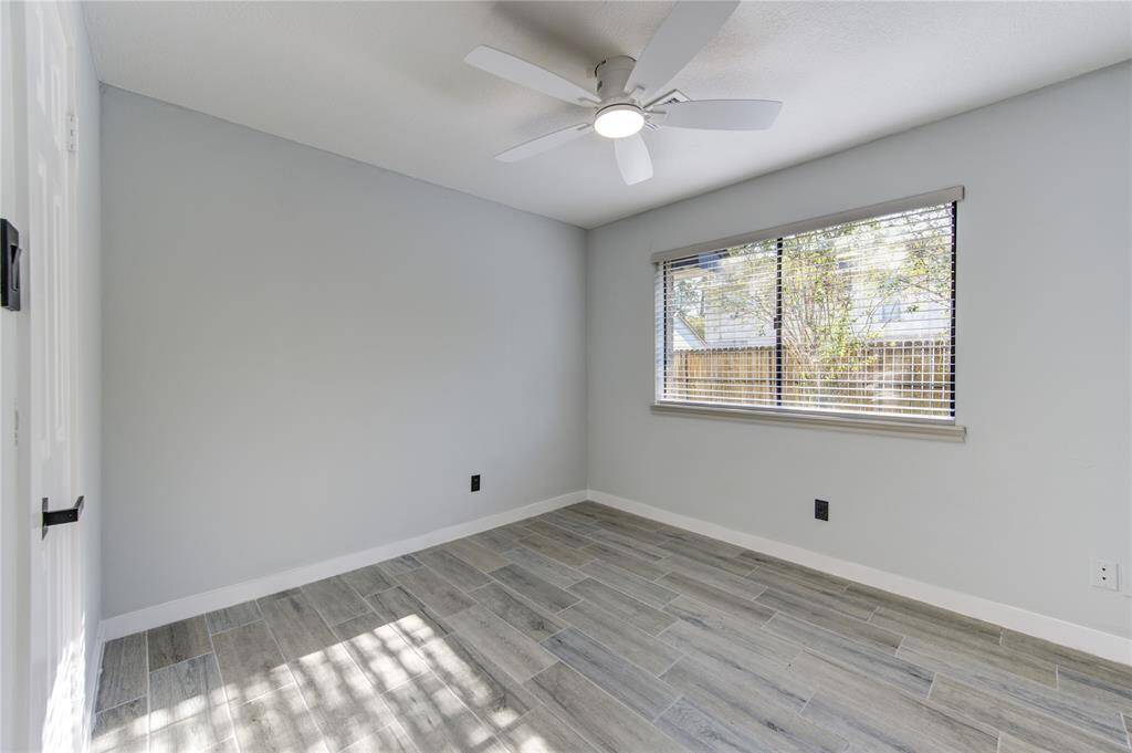 Bright and inviting bedroom featuring sleek flooring, a modern ceiling fan, and ample natural light from a large window.