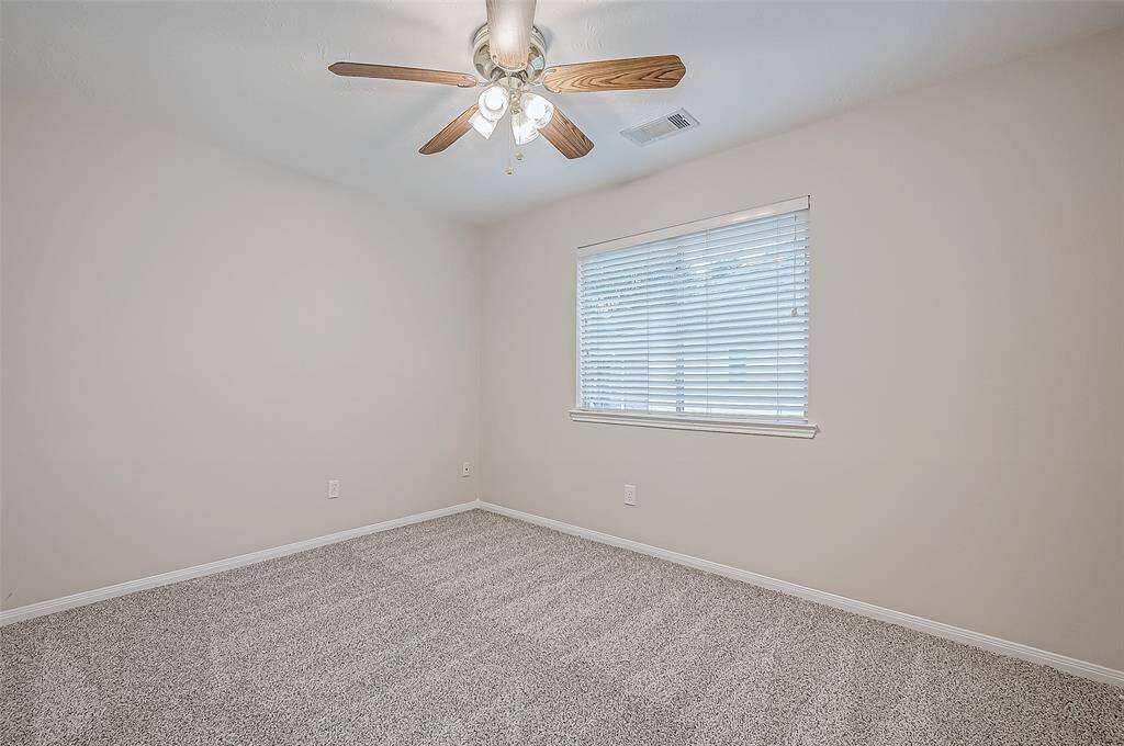 This inviting guest bedroom features soft plush carpeting, a bright window that fills the space with natural light, and a ceiling fan for year-round comfort.