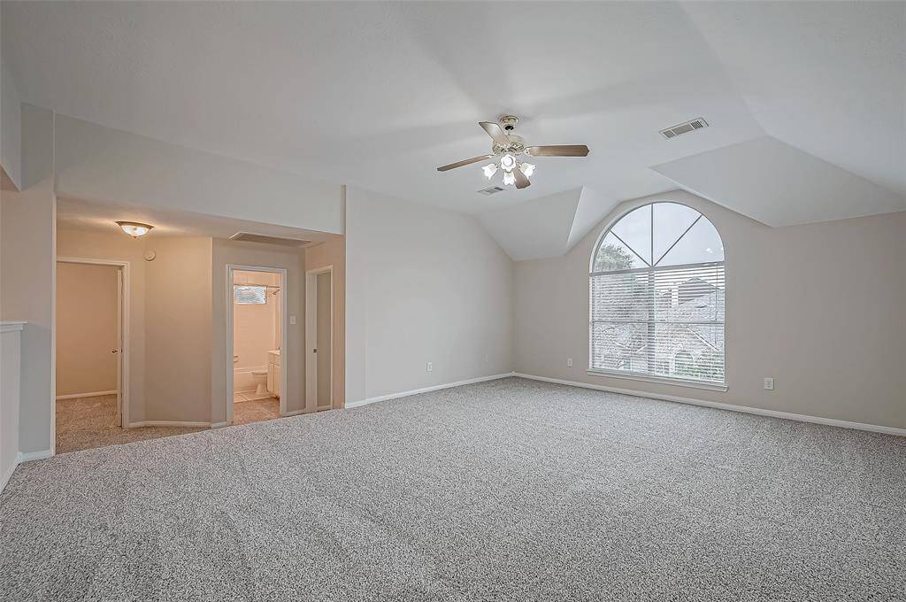 The open game room features a stunning arched window that bathes the room in natural light. The plush carpet and ceiling fan add comfort to the space.