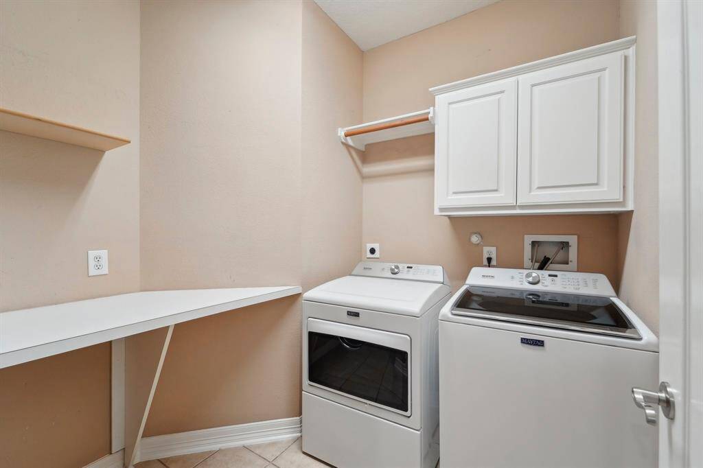 This well-appointed utility room features tile flooring, neutral paint, and both gas and electric dryer connections. Designed for convenience, it includes washer connections, built-in cabinetry for household storage, a hanging bar for clothes, and a spacious folding counter. Plus, the washer and dryer stay!
