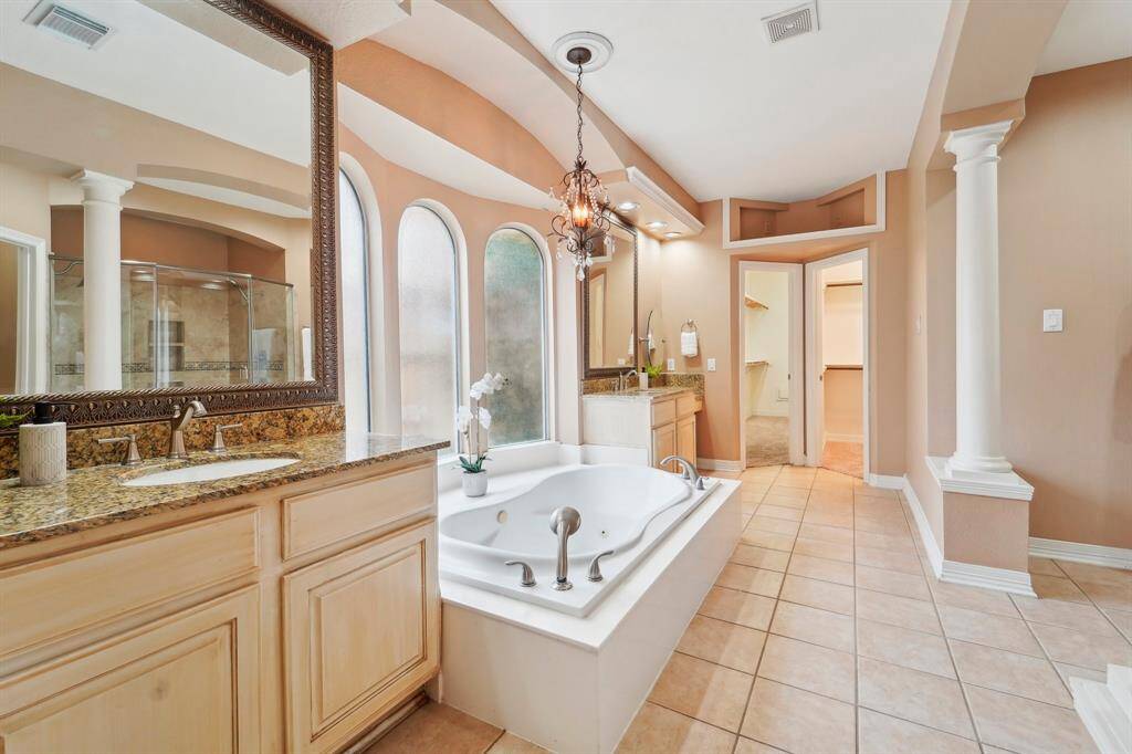 The owner's ensuite bathroom is thoughtfully designed for effortless sharing, featuring TWO spacious closets and dual vanities, each adorned with a custom-framed mirror and vanity lighting above. One vanity offers a dedicated knee space with extra lighting, creating a bright and comfortable area to get ready while seated on the included bench.