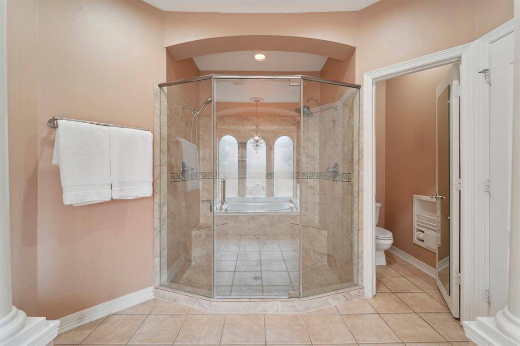 The oversized shower in the owner's retreat delivers a true spa-like experience, featuring dual shower heads, gorgeous tile work, frameless glass, and built-in benches for added comfort. Thoughtful details include a built-in magazine holder and a full-length mirror on the toilet room door, blending luxury with practicality.