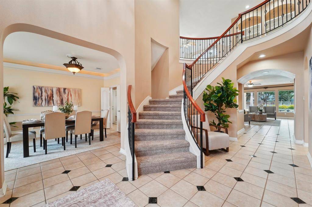 A grand, sweeping staircase creates a stunning first impression, complemented by elegant tile flooring, neutral paint, and a soaring two-story ceiling that enhances the sense of space. Thoughtful design elements invite you in, with glimpses of the formal dining room to the left, a private study to the right, and a breathtaking family room just ahead.