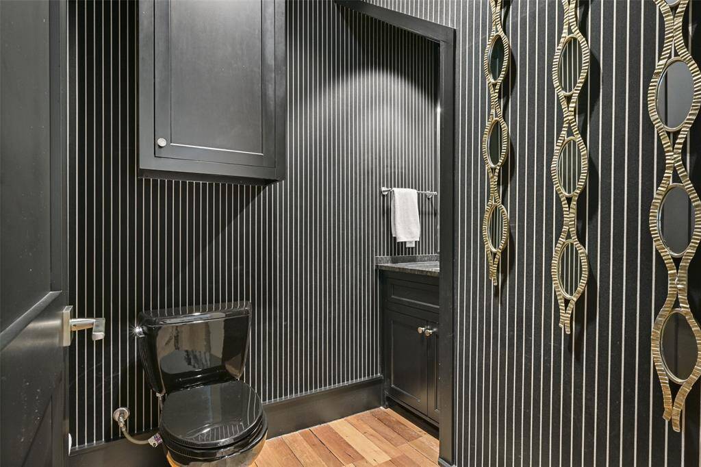 The half bathroom is designed with a bold & elegant aesthetic, featuring black and white wallpaper, black cabinetry & trim, that adds drama and enhances the luxurious ambiance.