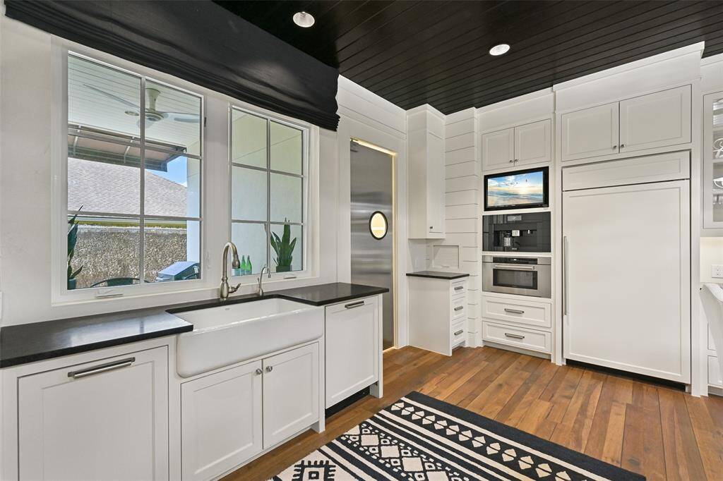 A large farmhouse sink overlooks a side patio area. While a built-in Miele coffee maker, Wolfe Microwave and Sub Zero Refrigerator/Freezer are built-in for a sleek & polished look.