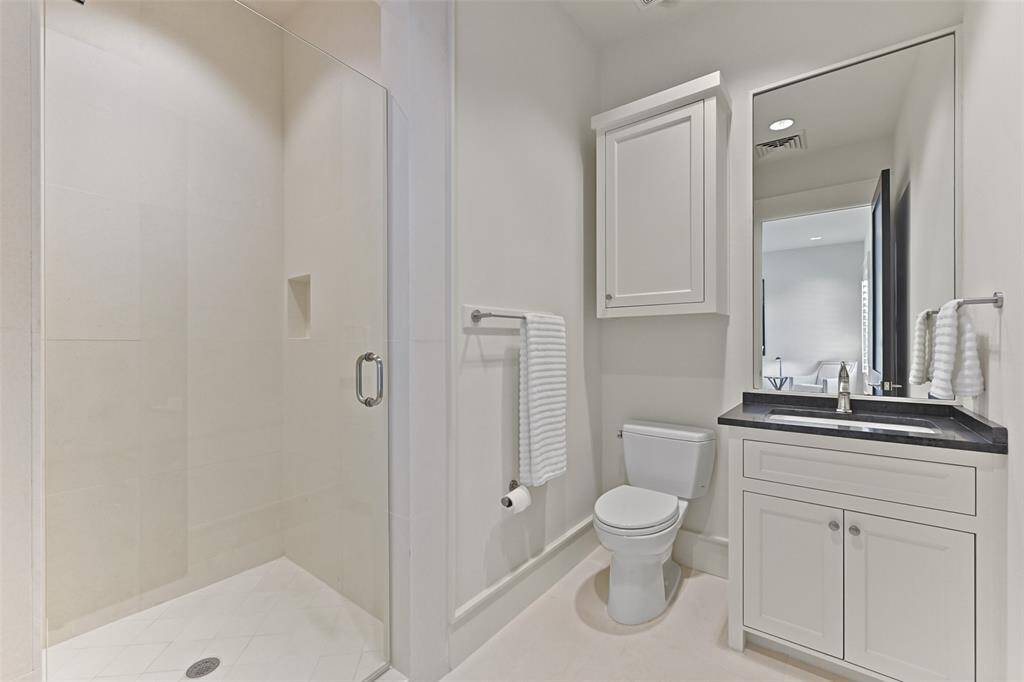 The ensuite bathroom for Bedroom 2 is designed with a sleek, clean and neutral aesthetic, featuring a walk-in shower and vanity with dark granite counters.