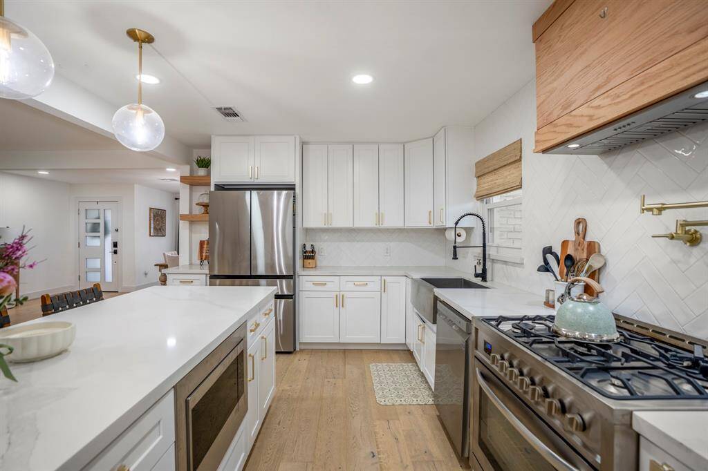 You will love the details of this kitchen! It features a large single basin sink with sleek faucet, brushed gold pot filler and cabinet hardware, wood paneled venthood, cream Zellige tile backspsh, and pendant lighting.