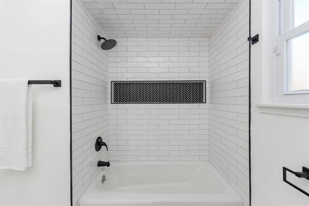 The spacious combination tub and shower is complete with a white tile surround, black accents and grount, and contrasting black plumbing hardware.