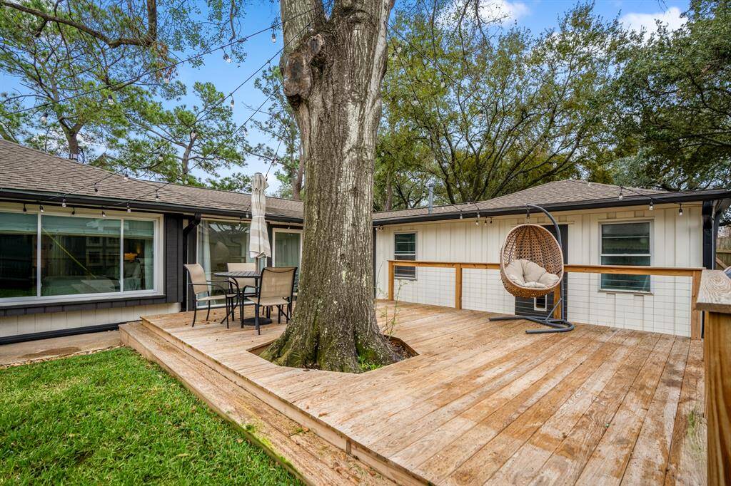 Outdoor living at its finest! This spacious backyard features a gorgeous wood deck shaded by a majestic tree, perfect for dining, entertaining, or relaxing. With lush green space and string lights for ambiance, this is the ultimate retreat right at home.