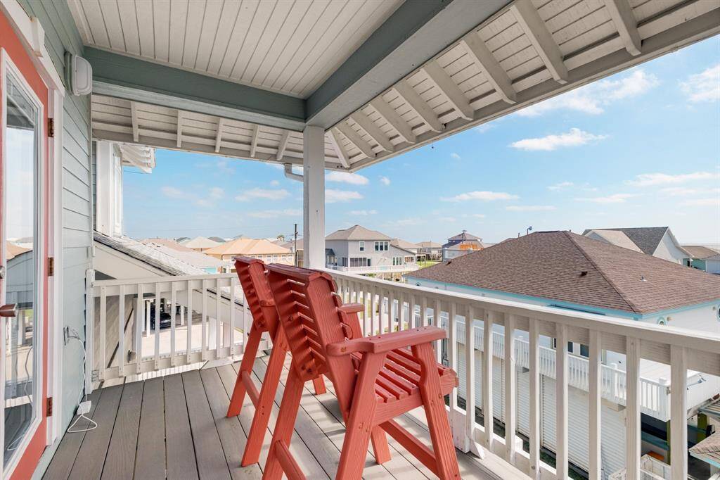 Cozy, covered balcony with seating for two red chairs provides a charming view of a neighborhood and peek a boo views of the beach.  Ideal for enjoying outdoor relaxation.
