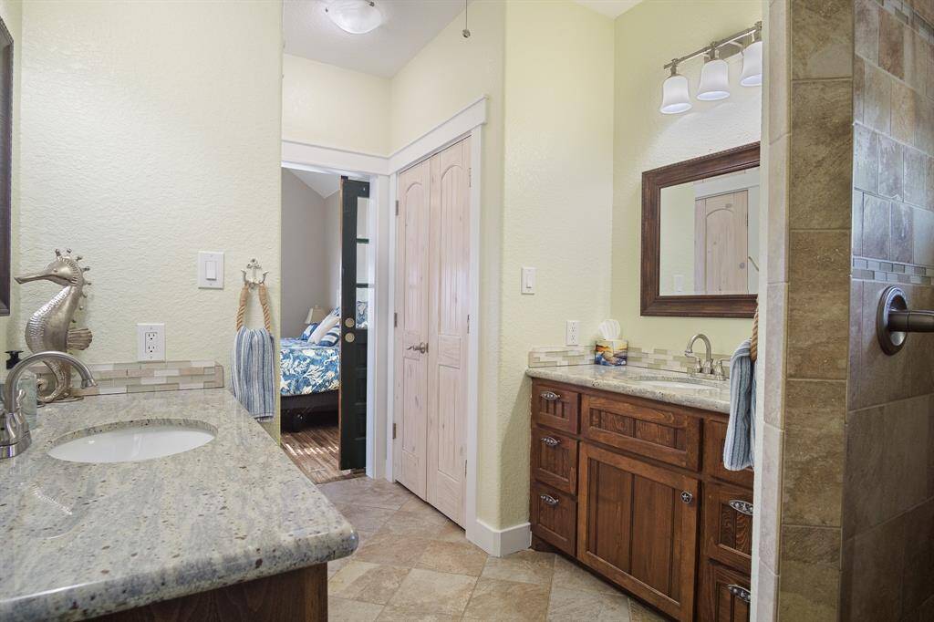 Private primary bathroom with dual-sink vanity with granite countertops and wood cabinetry. It has a walk-in shower with tiled walls and modern fixtures. The room is well-lit with overhead lighting and has a cozy, inviting atmosphere.