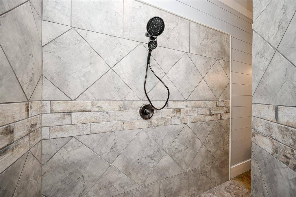 On the opposite side of the soaking tub is giant sized walk around shower complete with dual shower heads, full designer tile backsplash, and designer stone flooring.  Plenty of lighting and built in storage to hold toiletries are featured.