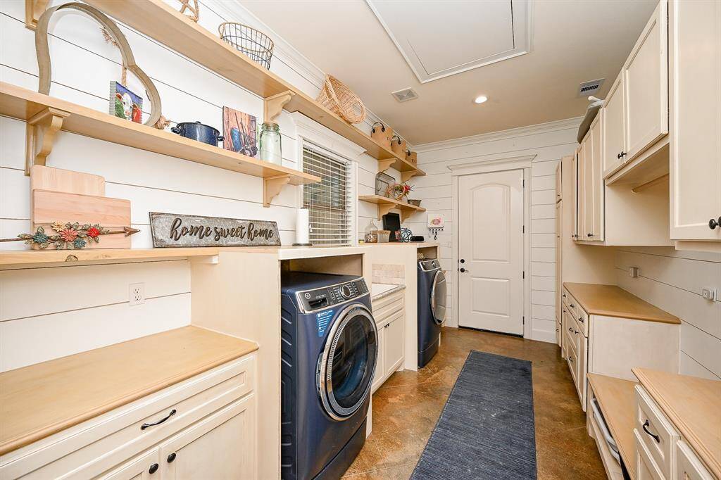 Continue thru the kitchen and you will come to a room which can double as the utility room and also a mud room.  Painted concrete flooring, plenty of shelving and cabinets for storage, recessed lighting and the same shiplap design are features.  The door allows for access to the 2-car garage.  A window allows for natural lighting and also look into the outside overhead patio and back yard.