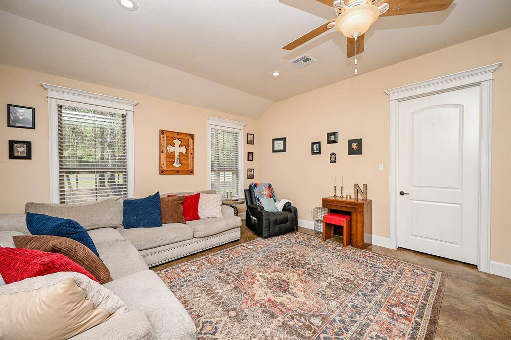 From the kitchen, enter the second living area and experience a large gathering area.  Two large windows allow for plenty of natural light to enter and offer views of the front yard.  Painted concrete flooring, ceiling fan, and recessed lighting are features along with the decorative molding and plantation-style blinds.