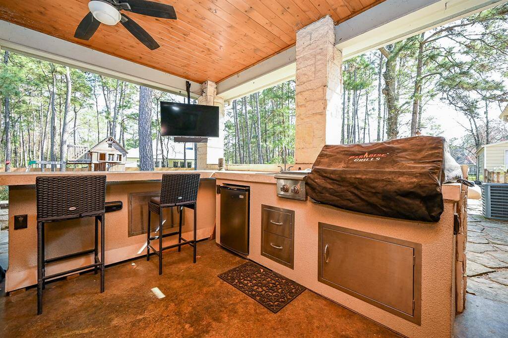 Like to entertain?  The outdoor covered patio allows you to do so.  The painted concrete flooring is carried outside.  This area features tile counter tops, outdoor grill, cook top, and sink to make food prep complete.  Its central location allows for a full view of the yard.  Designer wood ceiling complete with ceiling fan and stone constructed columns and counter facing add character.  Outdoor television screen adds to the entertainment value.