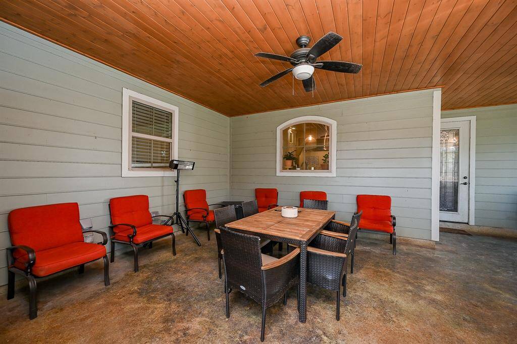 Talk about a large outdoor covered patio.  Outdoor gatherings need not be cancelled if the weather fails to cooperate.  This home features a large seating area, the same painted concrete flooring, designer wood ceiling, and ceiling fan.  The windows seen allow for viewing of the area from both the utility room and the interior kitchen, with the door, giving immediate access to the living area featuring the stone fireplace.