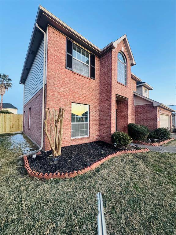 This two-story brick home features a classic design with large windows and a well-maintained front yard. It includes a small landscaped area and is complemented by a fenced backyard.