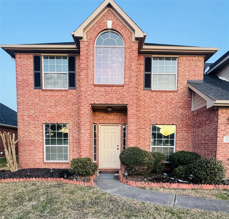 Charming two-story brick home featuring a grand arched window above the entrance, complemented by black shutters for a classic touch. The well-kept front yard and inviting pathway enhance its appeal.