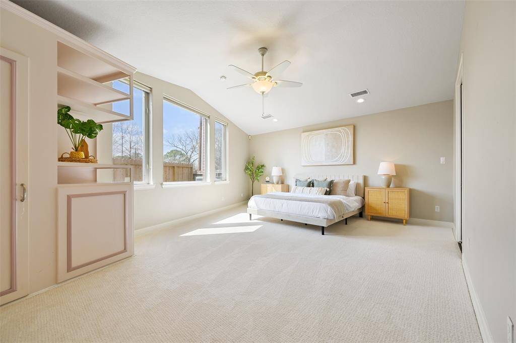 Experience luxury in the expansive first-floor master suite, featuring plush new carpet, neutral tones,  a lighted ceiling fan, recessed lighting, a large sunlit window, a built-in closet and shelves, and an en suite bathroom.