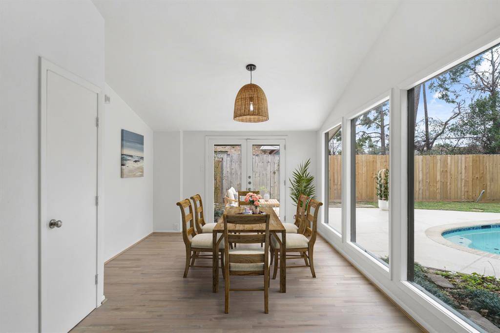 Just beyond the breakfast room, the formal dining room has a high ceiling with a hanging light fixture, a wall of plate glass windows overlooking the swimming & backyard and beautiful hardwood floors installed in 2024. This photo has been virtually staged.