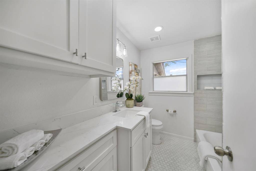The home's full bath includes upper & lower Shaker-style cabinets with a quartz surfaced counter top supporting an under-mount sink accompanied by wall mounted mirror & lighting. Included is recessed lighting, a window overlooking the backyard and tile flooring.