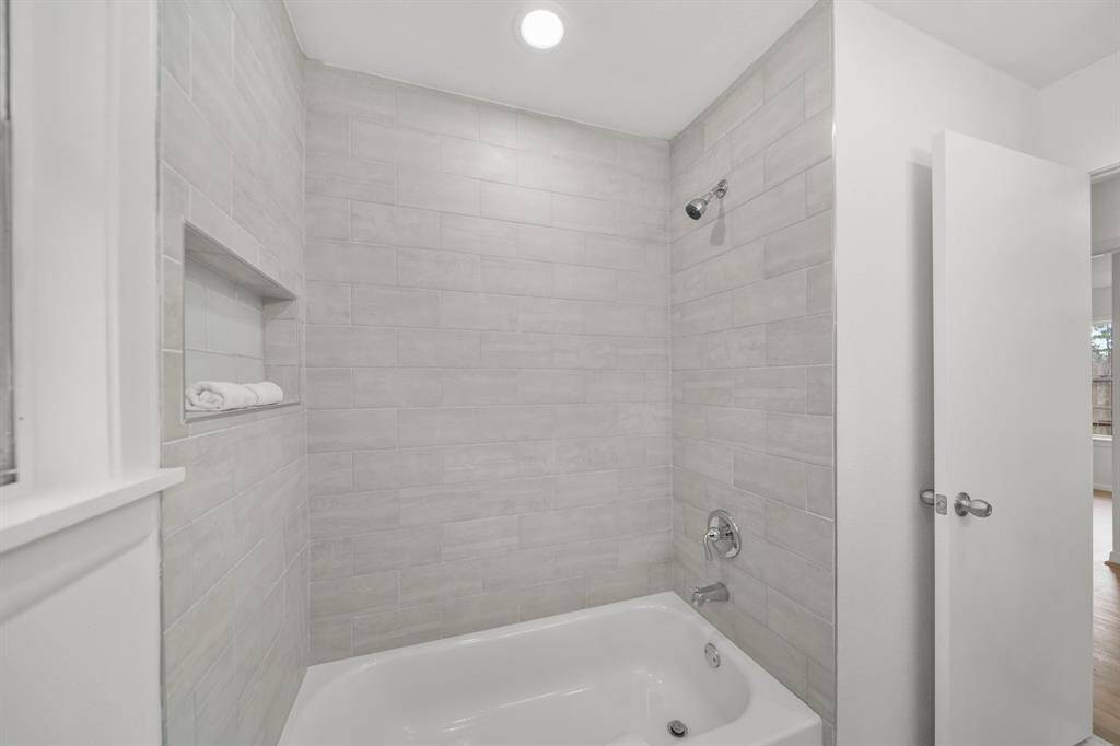 Relax & unwind in the floor-to-ceiling ceramic tile surrounded combination tub/shower with integrated soap/shampoo shelf & recessed lighting above.
