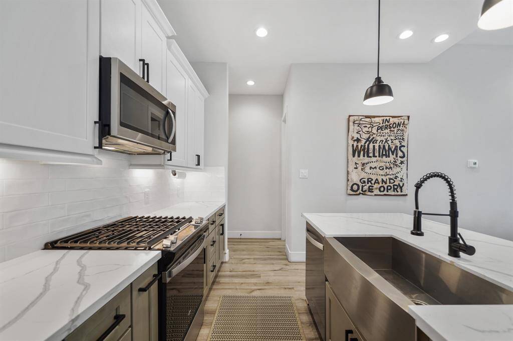 An under-mount stainless steel farm sink is included in the island & overlooks the dining & living rooms. Access to a half bath and the home's two-car attached garage is shown in the background.