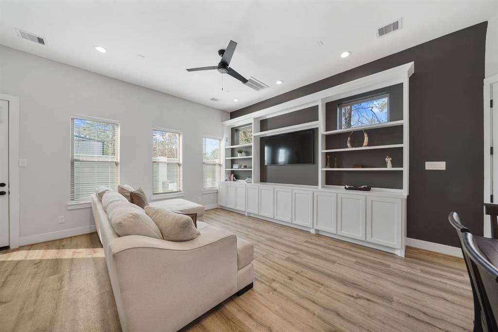 The living room sits on the back of the home with a high ceiling with recessed lighting, ceiling fan, pre-wiring for ceiling speakers & luxury vinyl plank hardwood flooring.