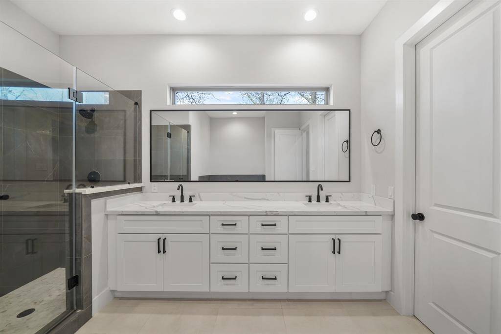 Features include recessed lighting, Shaker-style painted cabinets supporting a quartz counter top with dual under-mount sinks accompanied by a framed mirror & window above, a walk-in wardrobe closet, private water closet & tile flooring.