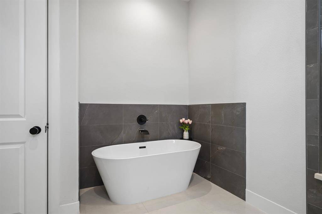 Relax & unwind in the freestanding soaking tub with black wall mounted plumbing fixtures surrounded by ceramic tile.
