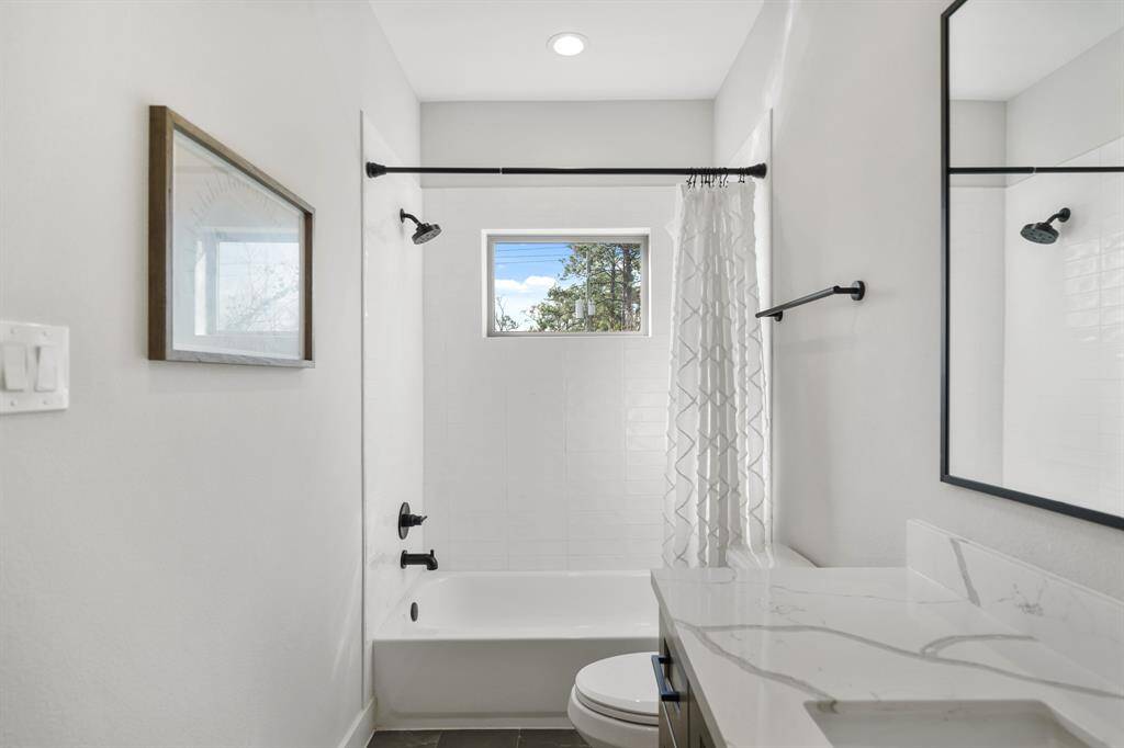 Serving as the home's second full bath, features include recessed lighting, a painted Shaker-style cabinet supporting a quartz counter top with integrated back splash and under-mount sink, a framed mirror & tile flooring.