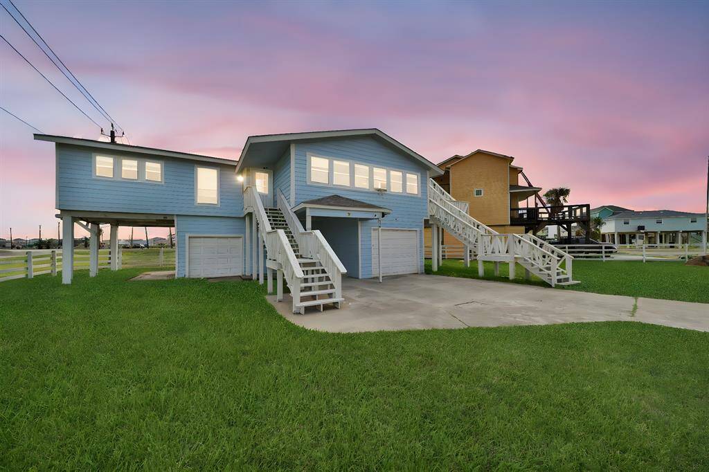 This elevated beach home features a modern design with large windows and a spacious exterior staircase. It includes a two-car garage and is set on a large, corner lot.