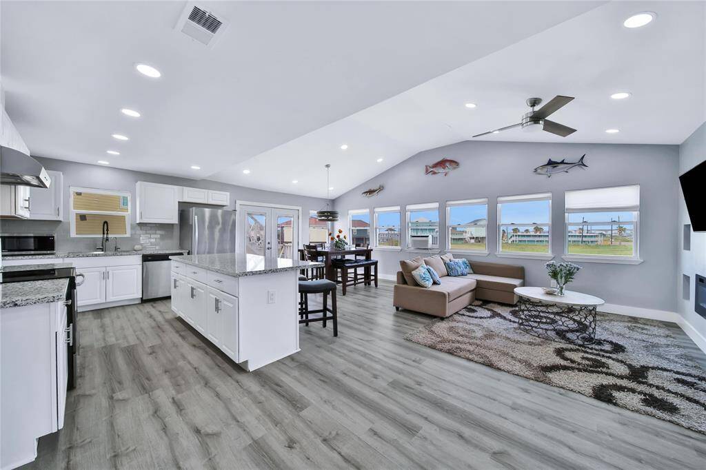 This open-concept living space features a modern kitchen with stainless steel appliances, granite countertops, and an island. It flows into a bright living area with large windows & stylish flooring. The dining area is conveniently located next to the kitchen, offering a perfect setup for entertaining.