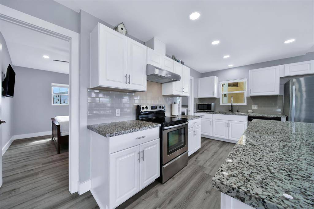 This kitchen features modern white cabinetry, granite countertops, and stainless steel appliances. It has a spacious layout with ample lighting.