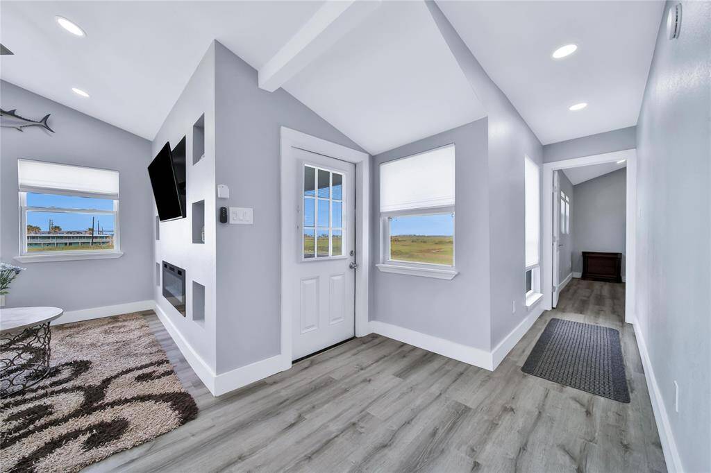 This bright, modern entryway features light gray walls, wood-look flooring, and recessed lighting. Large windows offer scenic views, and there's a wall-mounted TV and electric fireplace. It's a welcoming space leading to other rooms.