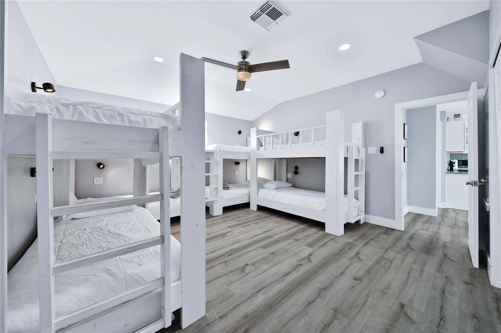 This spacious bedroom features sleek hardwood floors and is equipped with multiple white bunk beds, perfect for accommodating guests.