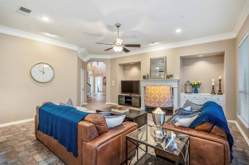 From the breakfast area, this view of the family room highlights the recessed alcoves on either side of the fireplace, each with built-in lighting to showcase art or decor. To the right of the fireplace, a built-in storage cabinet offers both functionality and style. On the left, an arched doorway provides a glimpse back toward the foyer and front door, connecting the space while maintaining an open, flowing layout.