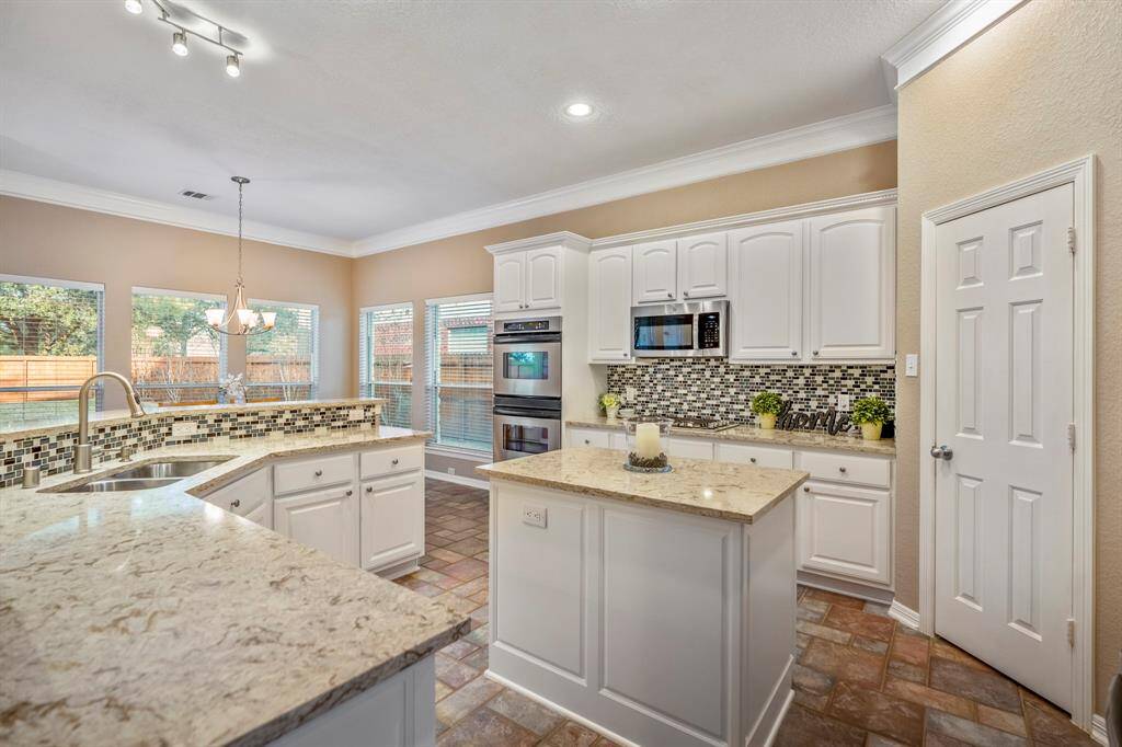 The kitchen is a true showstopper, featuring pristine white cabinetry with dental molding trim and sleek brushed nickel hardware. Sparkling quartz counters and a decorative mosaic tile backsplash create a stunning focal point. The kitchen is equipped with stainless steel appliances, including double ovens, a gas cooktop, and a built-in microwave. A spacious corner walk-in pantry offers ample storage, while the large center island with a wraparound bar creates a seamless divide between the living spaces.
