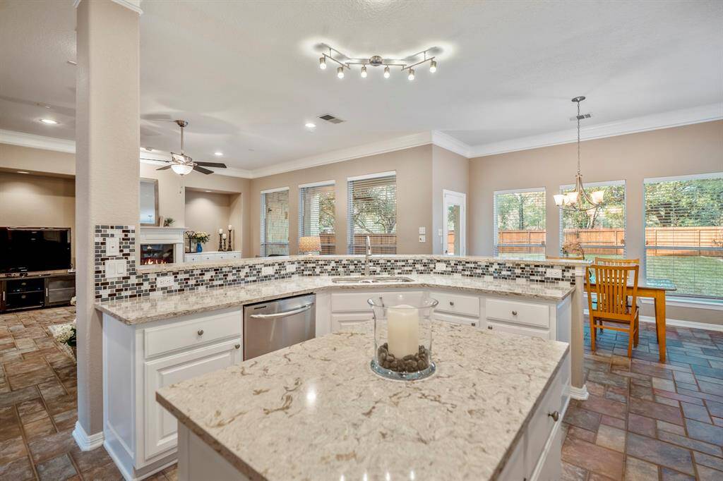 From the middle island, this view across the larger island to the living room and breakfast area showcases the thoughtful layout and ample storage in both islands. The dual-basin stainless steel sink with a pull-down faucet sits conveniently next to the dishwasher, making meal prep and cleanup a breeze. Modern lighting adds a contemporary touch, while the abundance of windows fills the space with natural light, creating a bright and welcoming atmosphere.