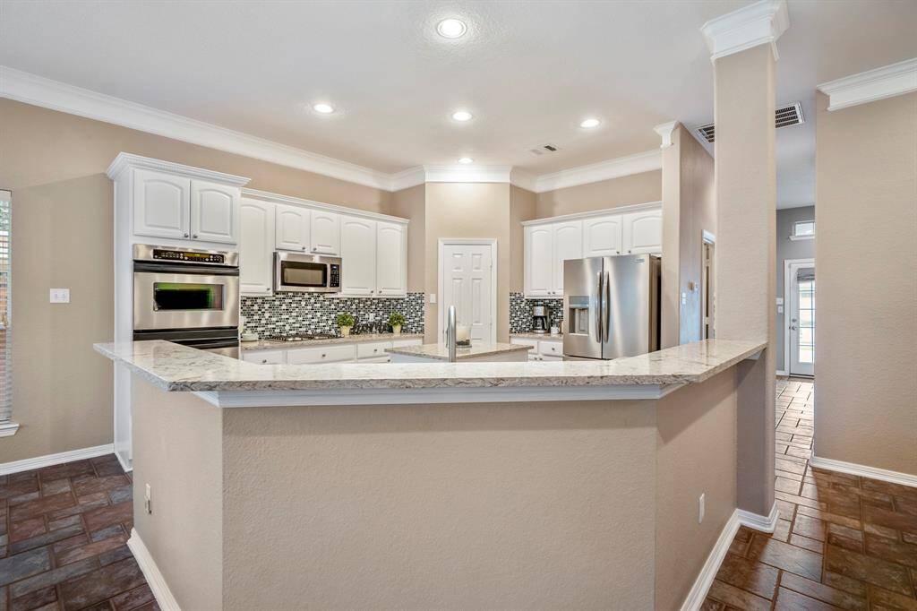 From the living room, looking into the kitchen, the raised bar creates a natural flow between the two spaces. The sleek design of the kitchen is complemented by a view down the hallway to the right, where the second entrance door leads out to the driveway, adding both convenience and ease of access.