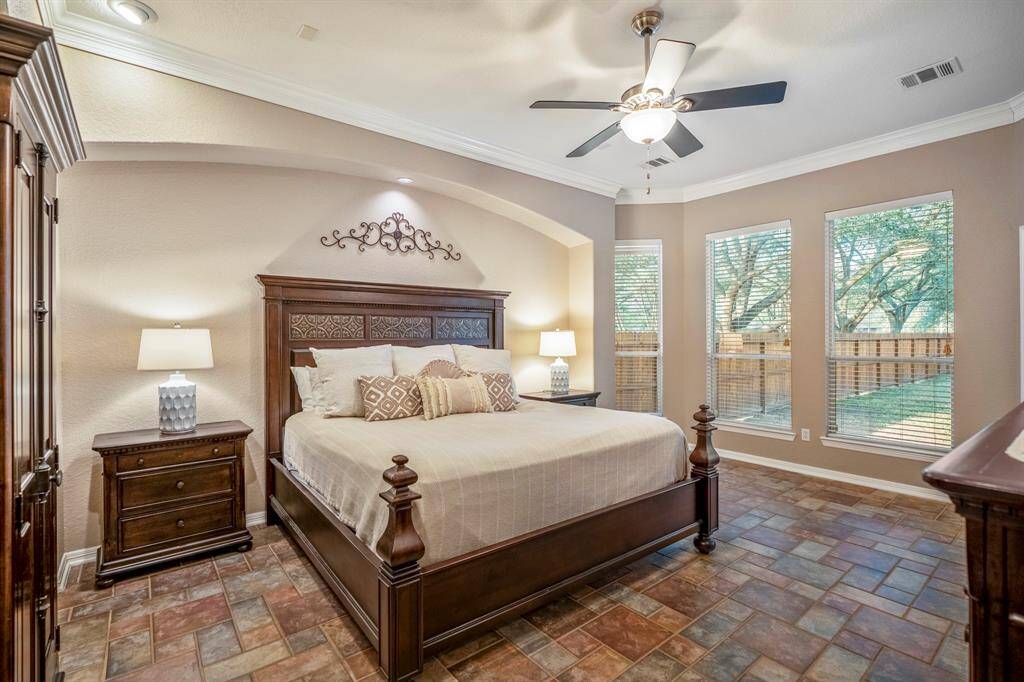 The spacious primary bedroom is a serene retreat, featuring a recessed archway behind the bed that adds architectural charm. Bay windows fill the room with natural light, while tile flooring and crown molding enhance the elegant design. A perfect blend of style and comfort.