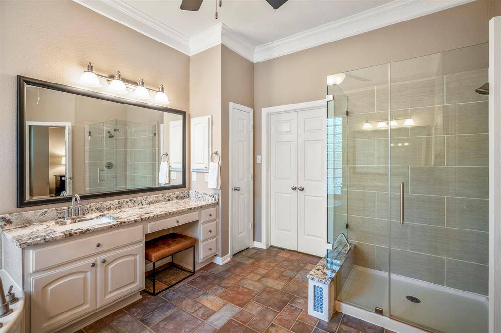 This view highlights the right side of the primary bath, showcasing the frameless glass-enclosed shower and the linen closet conveniently located next to the vanity. The double doors lead into the spacious walk-in closet, thoughtfully designed with triple rows for clothing and built-in shelving for effortless organization.