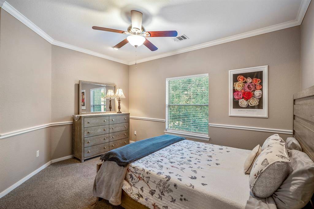 This spacious bedroom off the game room features elegant chair railing and crown moulding, adding a touch of sophistication. A large window overlooks the backyard, bringing in natural light and offering a peaceful view.