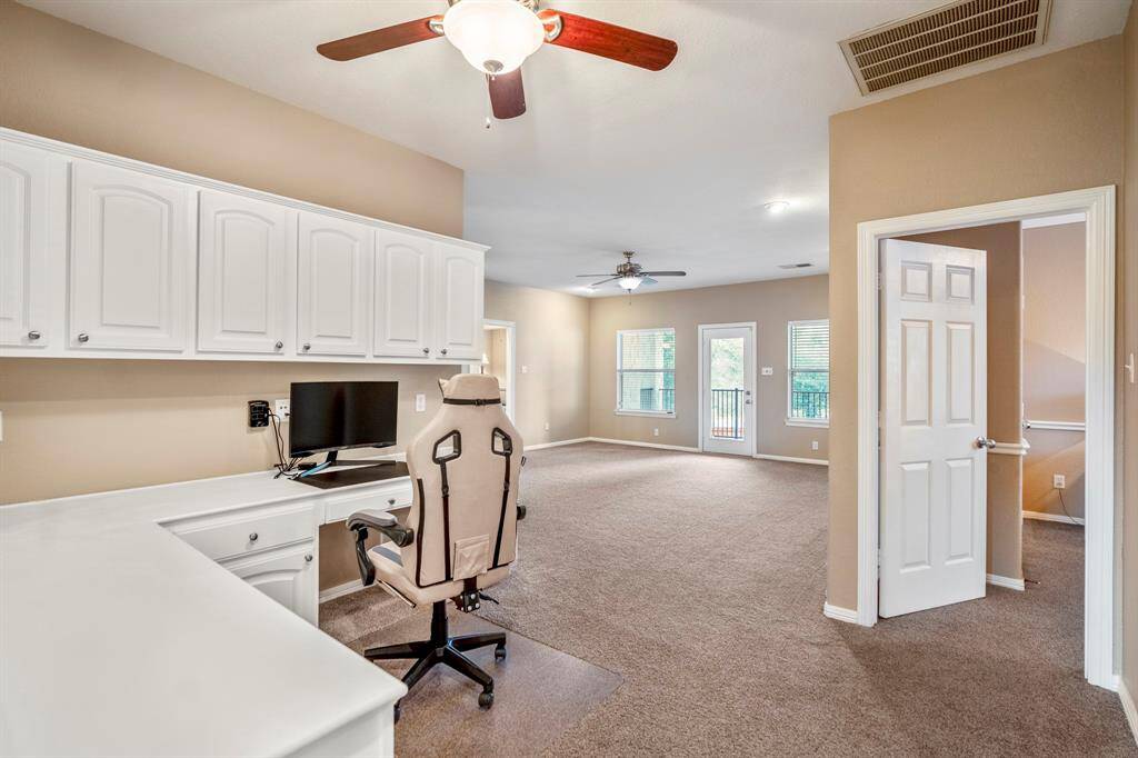A closer view of the built-in desk area in the game room shows a practical workspace with plenty of storage. In the distance, you can see the windows and door leading to the balcony. To the right, the photo captures a glimpse into another bedroom, offering privacy and easy access from the game room.